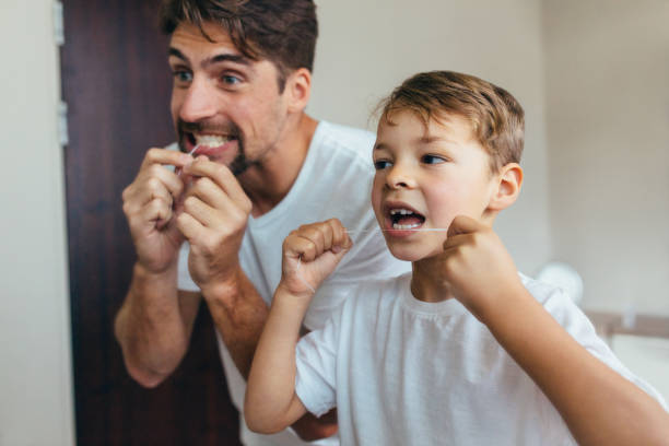 père et fils, nettoyer les dents avec la soie dentaire - son photos et images de collection