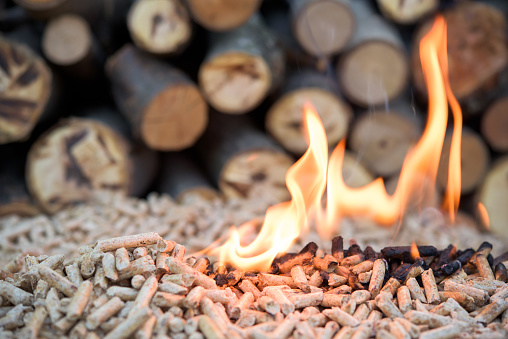 A wicker basket of birch logs on a timber stump against the background of a fireplace with burning firewood.