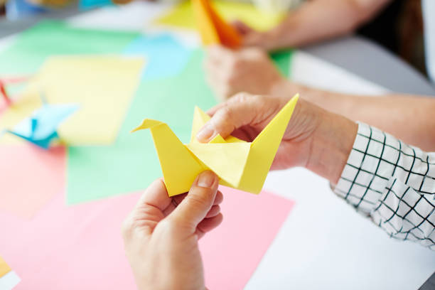 Making paper bird Human hands folding sheet of yellow paper while making origami bird origami stock pictures, royalty-free photos & images