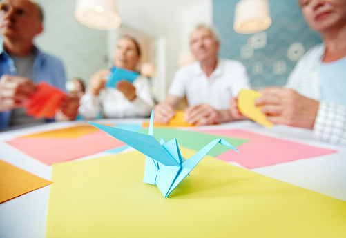 Several humans learning how to make paper origami with blue figure on table