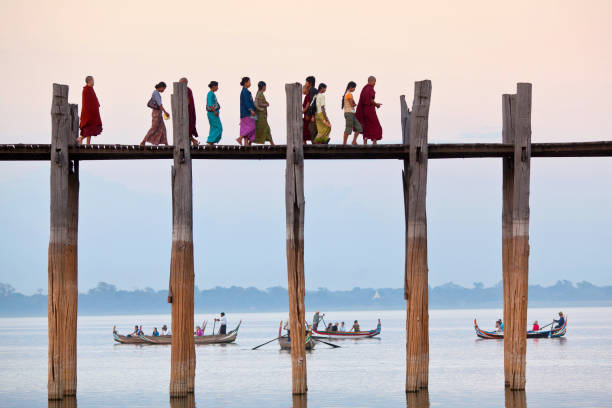 U-Bein teak bridge on Taungthaman lake in Mandalay division, Myanmar Amarapura, Myanmar - January 11, 2011: People walking on famous ancient U-Bein teak bridge on Taungthaman lake in Mandalay division u bein bridge stock pictures, royalty-free photos & images