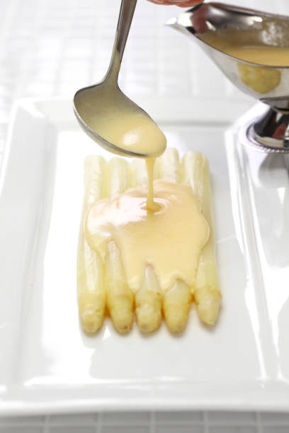 Hollandaise sauce is poured over white Asparagus. white asparagus with hollandaise sauce hollandaise sauce stock pictures, royalty-free photos & images