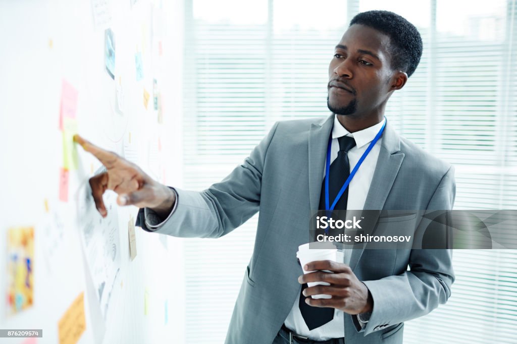 Reading points of plan Confident policeman in suit and tie pointing at message on notepaper on whiteboard African-American Ethnicity Stock Photo