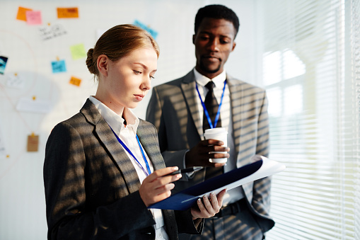 Youing female agent reading paper with important information with colleague near by