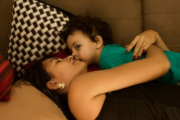Mother and her little son, lying down in a couch with affectionate gesture.