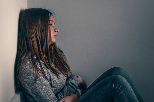 Sad girl sitting on the floor in corner of room,  portrait of a sad teenage girl looking thoughtful about troubles. Depressed teenage girl. Lonely Depressed Teen Girl. Unhappy depressed teenager