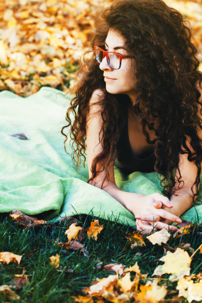 молодая женщина, лежащая в парке и наслаждающаяся хорошей погодой - glasses grass women lying on front стоковые фото и изображения