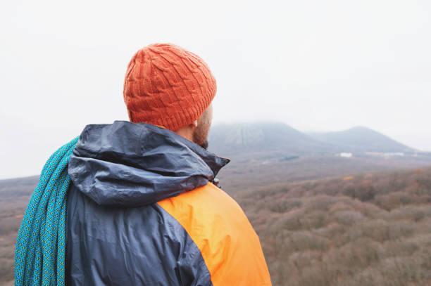 istock Hipster-climber stands in a down jacket on a rock with a rope on his shoulder 876309700