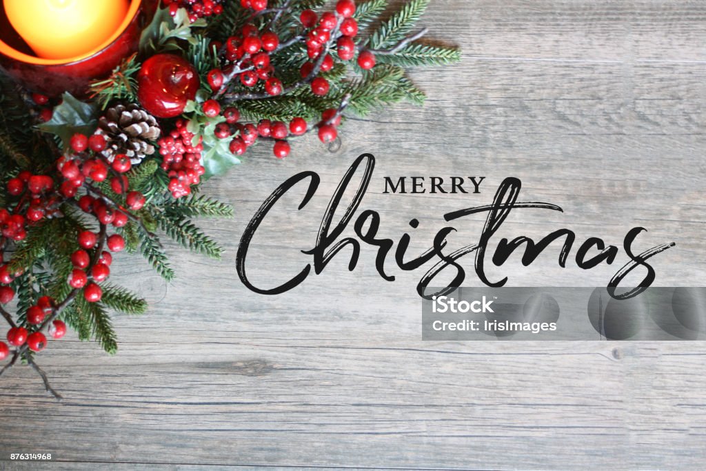 Merry Christmas Text, Candle, Pine Tree Branches and Berries in Top Corner Over Rustic Wood Merry Christmas Text, Festive Holiday Candle, Pine Tree Branches and Berries in Top Corner Over Rustic Wood Background Christmas Stock Photo