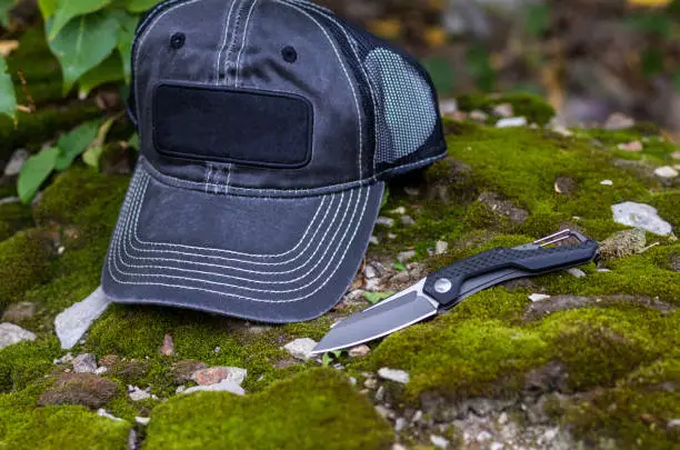 Photo of Black folding knife and black baseball cap.