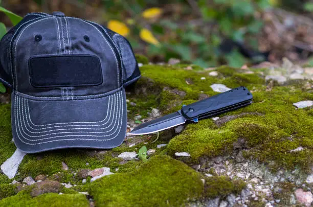 Photo of Black knife and black cap. Folding knife and baseball cap.