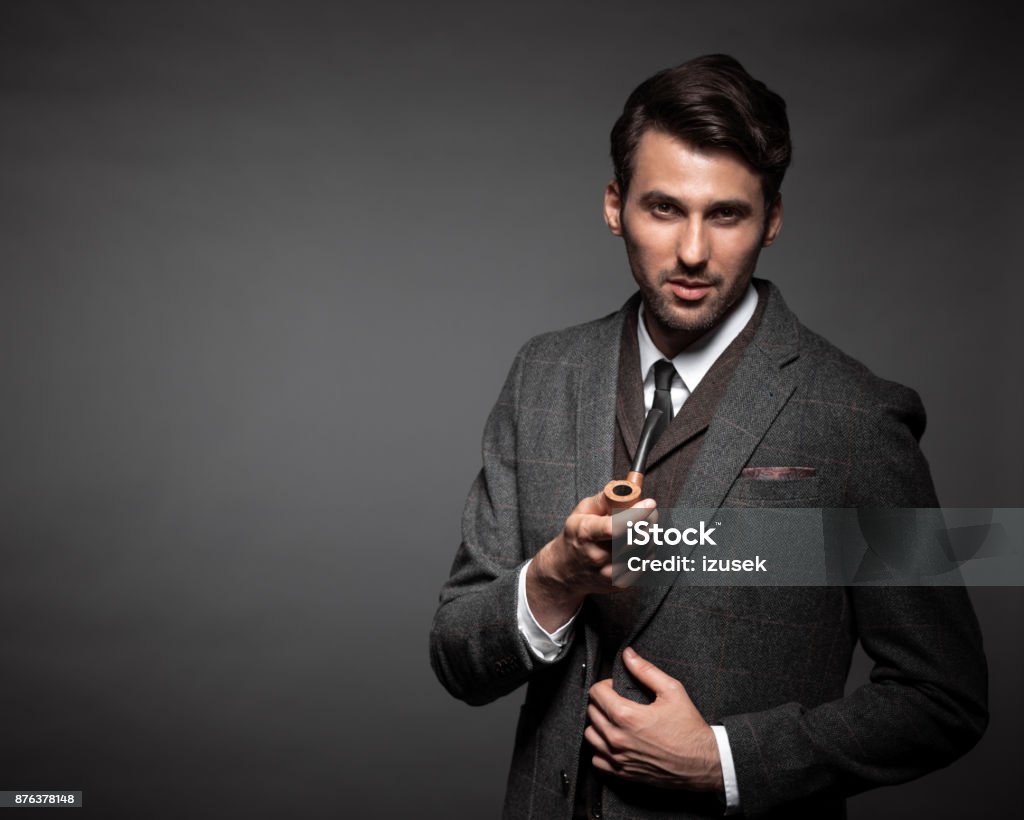 Handsome man with a smoking pipe Portrait of handsome young man in suit with a smoking pipe standing against dark background. Suit Stock Photo