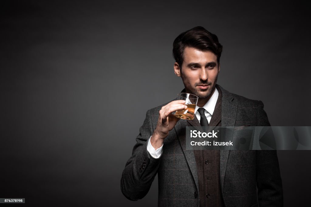 Portrait of handsome man drinking whiskey Portrait of handsome man drinking whiskey in studio. Business man with glass of whiskey looking away on black background. Whiskey Stock Photo