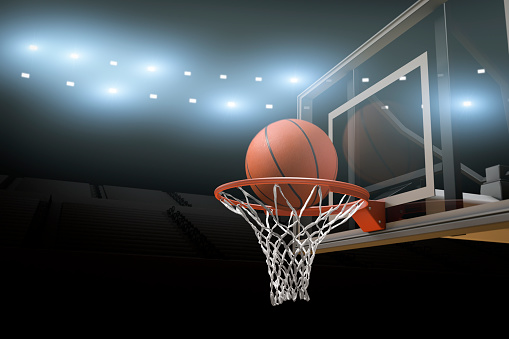 A basketball going through a basketball goal mid air in  professional basketball stadium or arena with stadium lights and flares and copy space for text.