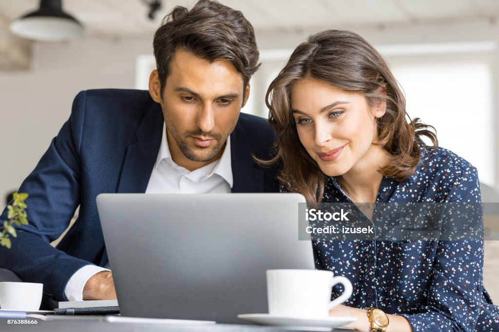 Couple of business people working on laptop at cafe Couple of young business people looking at laptop. Businessman and businesswoman sitting at cafe table and working together on laptop computer. Advice Stock Photo