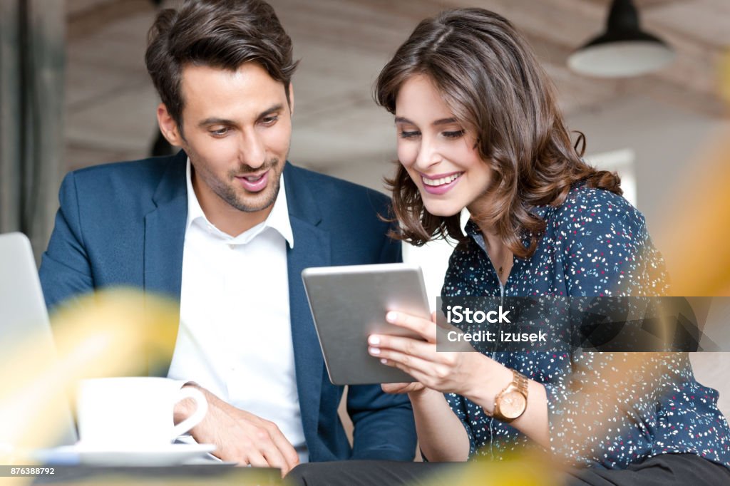 Couple of young business people looking at digital tablet Smiling business people meeting in a coffee shop looking at digital tablet. Businesswoman showing something to businessman on digital tablet. Digital Tablet Stock Photo