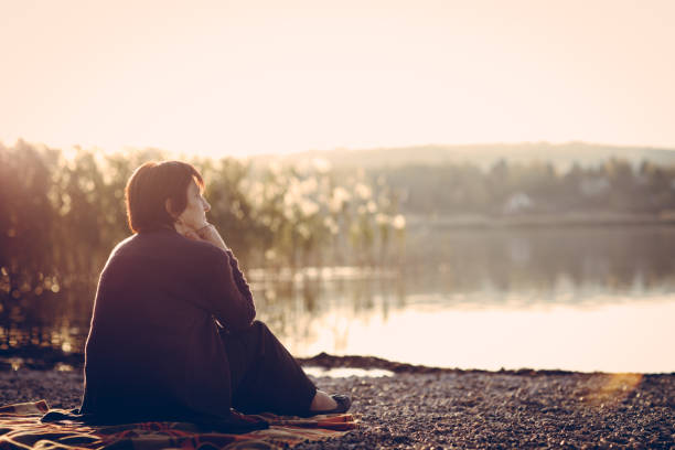istock Senior woman sitting on a lake shore 876394144