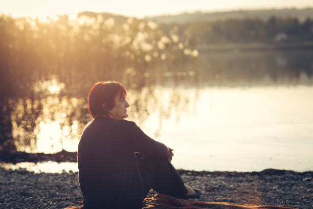 istock Senior woman sitting on a lake shore 876394170