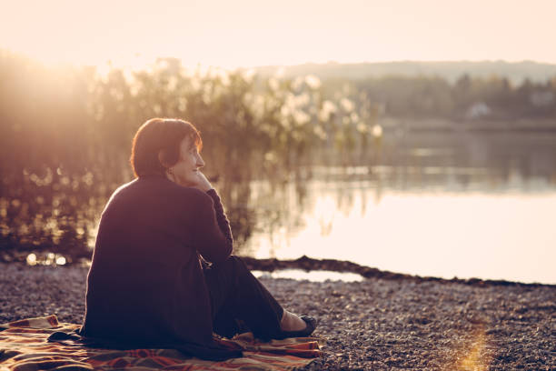 istock Senior woman sitting on a lake shore 876394196