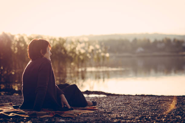 istock Senior woman sitting on a lake shore 876394230