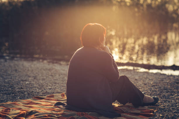 istock Senior woman sitting on a lake shore 876394270