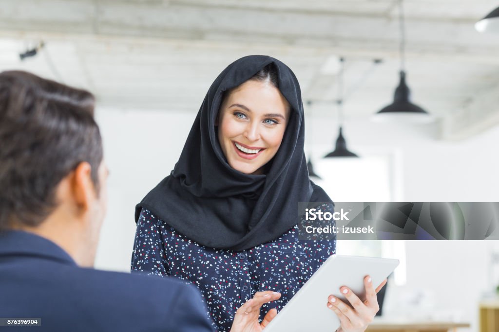 Happy businesspeople discussing work Muslim businesswoman holding digital tablet and talking with male colleague in office. Happy businesspeople discussing work. 20-29 Years Stock Photo