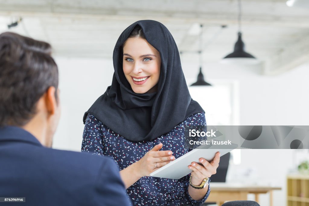 Muslim businesswoman in discussion with colleague Muslim businesswoman holding digital tablet and discussing work with businessman in office. Businesspeople discussing new project. Digital Tablet Stock Photo