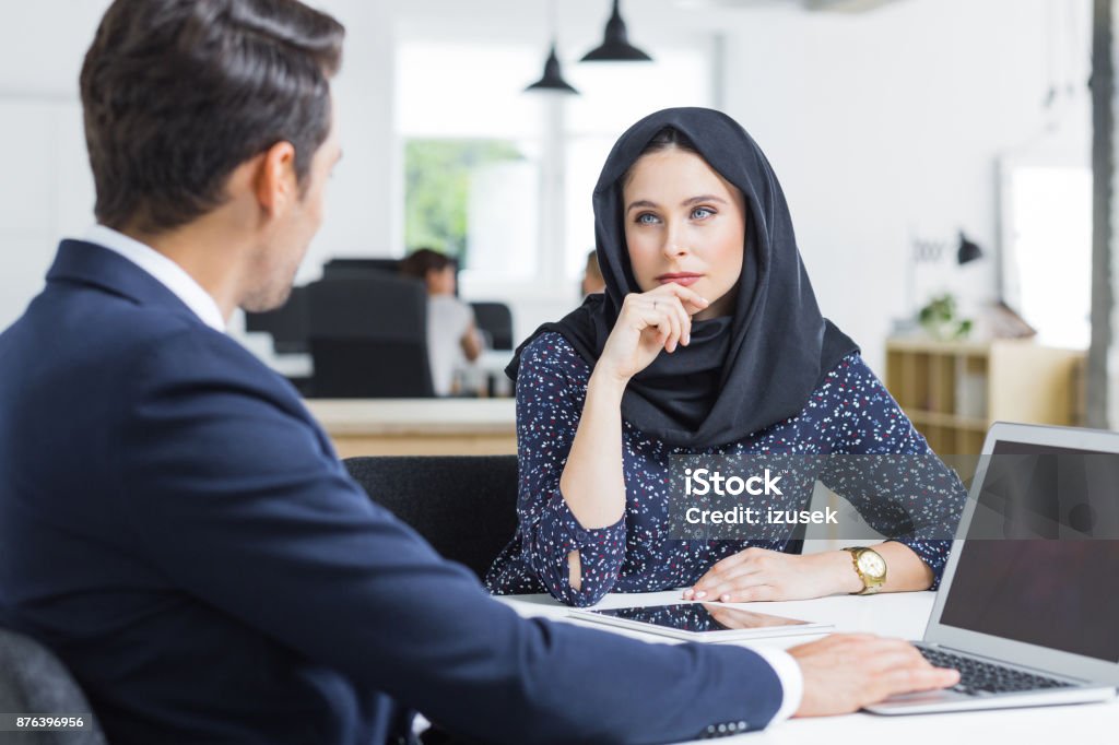 Muslim businesswoman working listening to male colleague in office Muslim businesswoman sitting at table and listening to male colleague. Professional employees discussing ideas for new business project in office. Listening Stock Photo