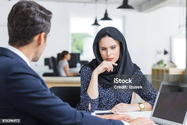 Serious Businesswoman At Desk With Male Colleague Stock Photo - Download Image Now - Office, Islam, Introspection