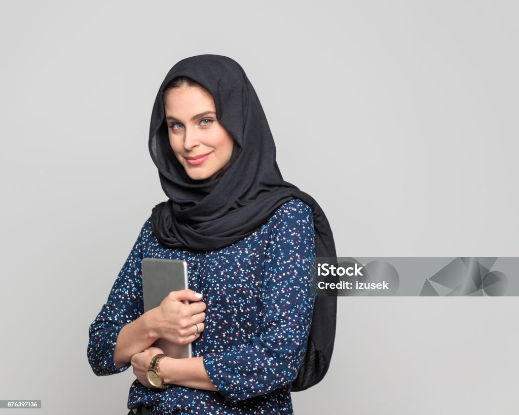 Modern arabic woman with digital tablet Portrait of beautiful muslim woman holding digital tablet and looking at camera. Businesswoman in hijab standing against grey background. Headscarf Stock Photo