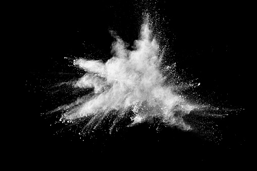 Freeze motion explosion of white dust on  black background. By throwing talcum powder out of hand. Stopping the movement of white powder on dark background.