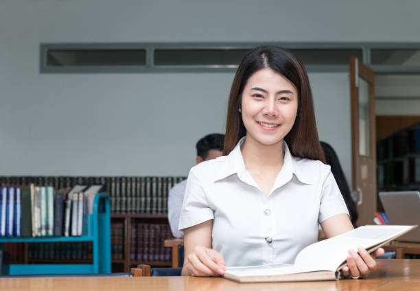 istock cute asian student reading book in library university 876420252