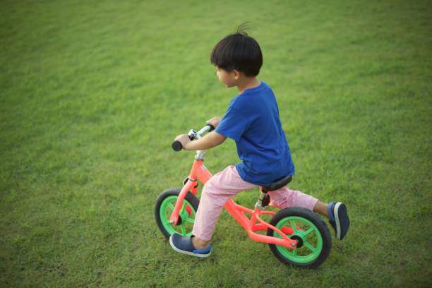 Little boy riding a balance bike on grass : soft focus stock photo
