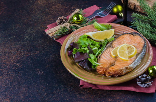 istock Christmas Dinner Table Setting. Delicious salmon steak grilled on plate with lemon and assorted salad on dark stone table background. Top view, copy space 876434844