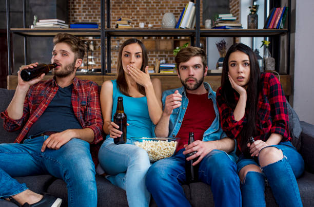 um grupo de amigos modernos dos alunos assistir um filme de terror na tv, beber cerveja e comer pipoca enquanto está em casa sentado no sofá. - entertainment center watching tv television popcorn - fotografias e filmes do acervo