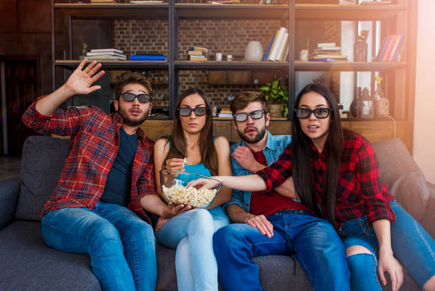 uma empresa de jovens amigos comendo pipoca assistindo um filme de terror em 3d óculos sentado no sofá na frente da tela em casa - entertainment center watching tv television popcorn - fotografias e filmes do acervo