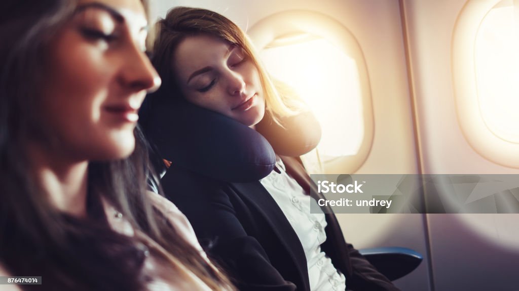 Girlfriends traveling by plane. A female passenger sleeping on neck cushion in airplane. Girlfriends traveling by plane. A female passenger sleeping on neck cushion in airplane Airplane Stock Photo