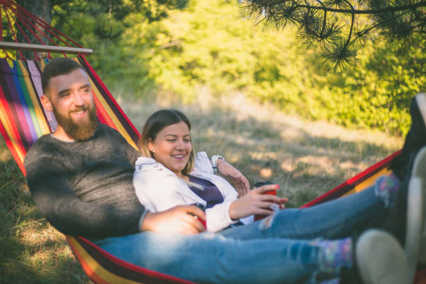 istock Young man and girl in orange hammock from back in beautiful forest 876486496