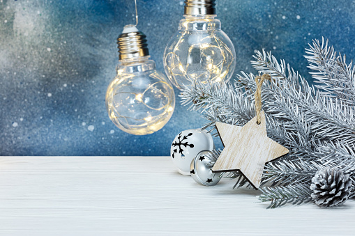silver christmas fir tree branch, tree decorations and glowing retro light bulbs on blue background