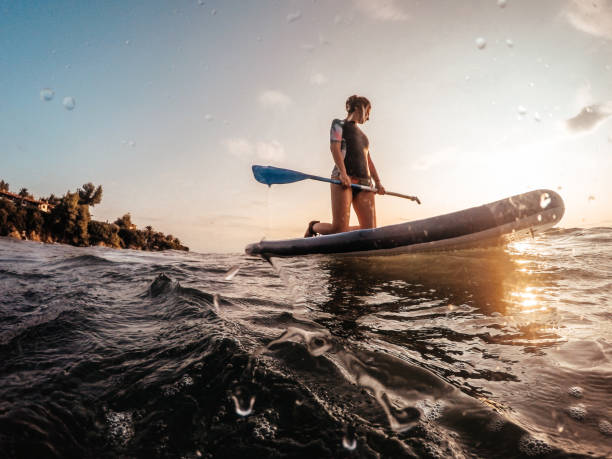 Young woman on a paddle board Photo of a young woman floating in the ocean on her paddle board  at sunset paddleboard photos stock pictures, royalty-free photos & images