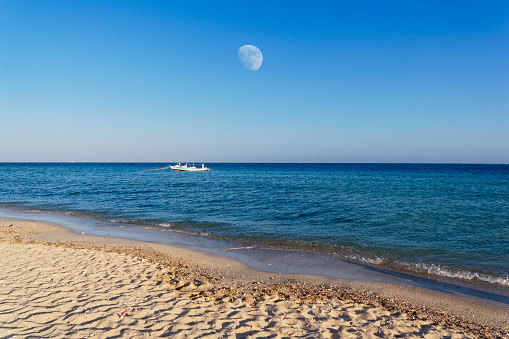 Moon rising over the Red Sea just before sunset. Two local fising boats moored close to the beach.