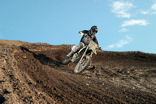 Motocross enduro rider in action accelerating the motorbike after the corner on dirt race track. Extreme off-road race. Hard enduro motorbike. Sky on background