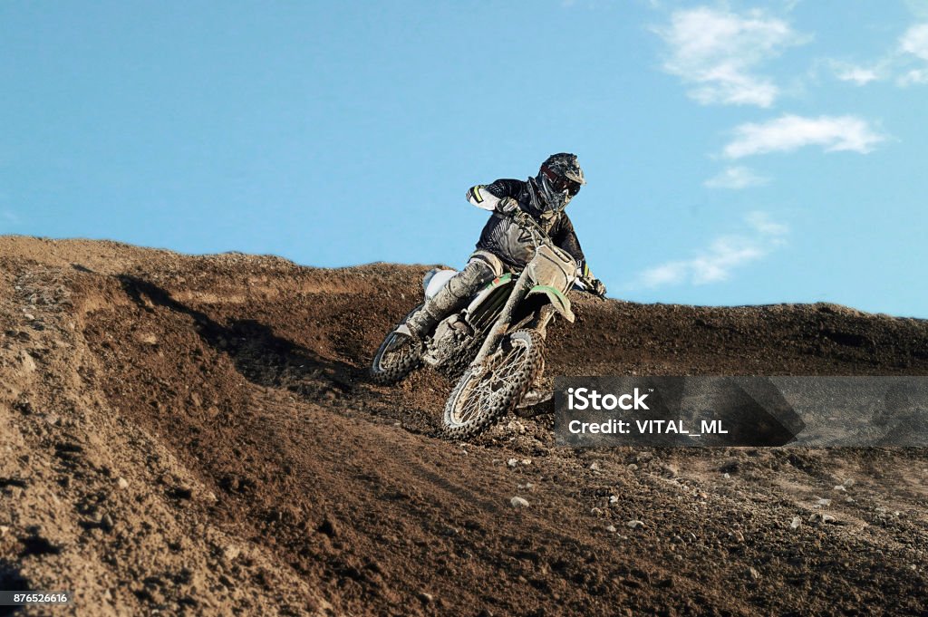 Motocross rider on race track Motocross enduro rider in action accelerating the motorbike after the corner on dirt race track. Extreme off-road race. Hard enduro motorbike. Sky on background Motorcycle Stock Photo