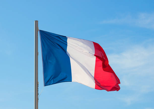 istock French flag fluttering in a brisk breeze against a bright blue sky in summer background. 876538664