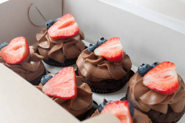 istock Chocolate cupcakes with whipped chocolate cream, decorated fresh strawberry, blueberry on white background in box. 876538742