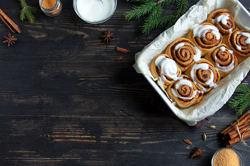 Cinnamon rolls or cinnabon for Christmas. Homemade traditional winter festive dessert buns pastry on dark wooden background with copy space.