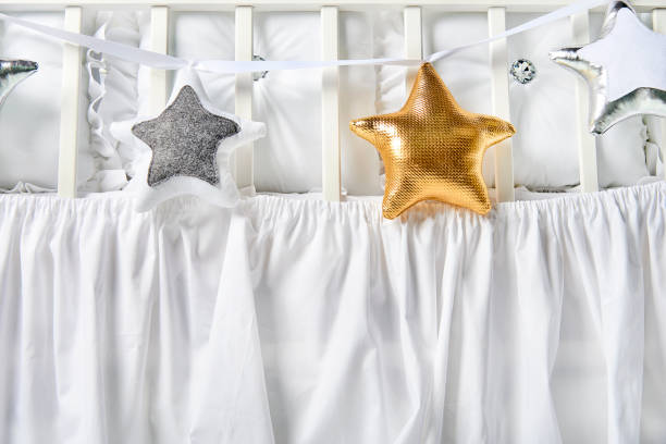 istock Silver, gold and white star shaped pillows on a white baby cot 876551308