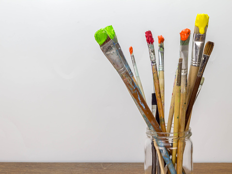 Photo of dirty paint brushes in glass jar on wooden table