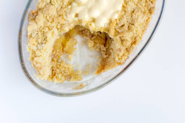 Cooked cinnamon apple crumble pie in glass oval dish on white background - Top view