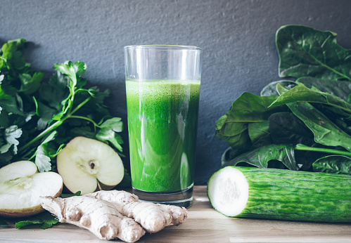 fresh green healthy detox juice in glass surrounded by vegetables and fruits